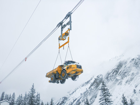 A 20-ton dump truck is being transported via a heavy crane system at the 360-MW Obervermuntwerk II project in Austria during heavy snows in the Alps.